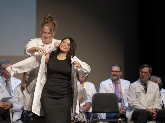 Professor Jennifer Hunter in the University of Arizona College of Nursing, helps Xitlali Arias-Ortiz into her coat at the college’s white coat ceremony.