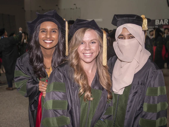 Three young women wearch graduation caps and gowns smile.