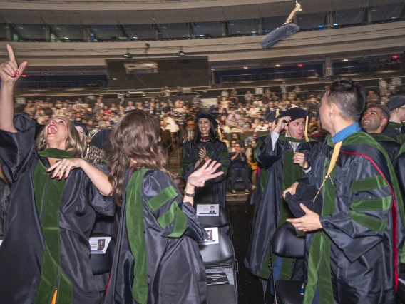 A large group of medical students wearing graduation regalia celebrate by throwing their hats into the air.