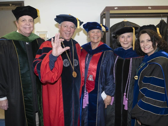 Five university leadership and faculty members dressed in graduation regalia smile before taking the stage in Centennial Hall.