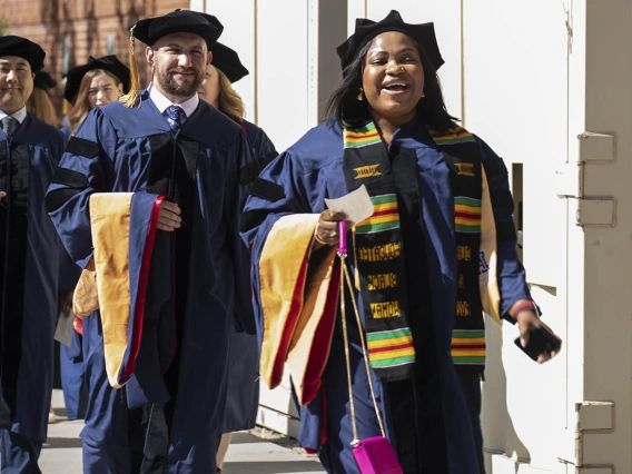 Two men and one woman dressed in graduation cap and gowns proceed into Centennial Hall for convocation.