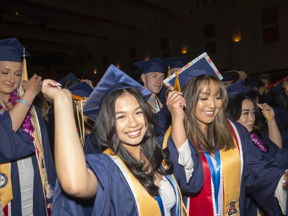 Two young women smile as they move their graduation cap tassle to the other side to signify their graduation.