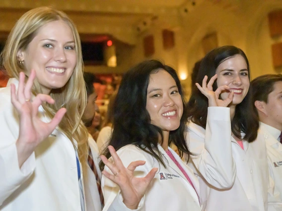 Three female medical students in white coats smile while holding up their hands make the Arizona Wildcat sign.