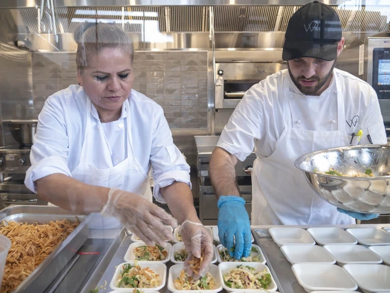 Two chefs in white coats prepare small salad plates in a kitchen. 