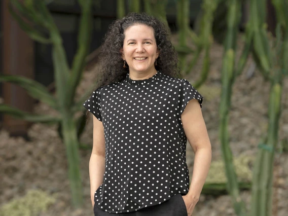 Portrait of woman with dark, curly hair. She is wearing a black top with white polka dots.