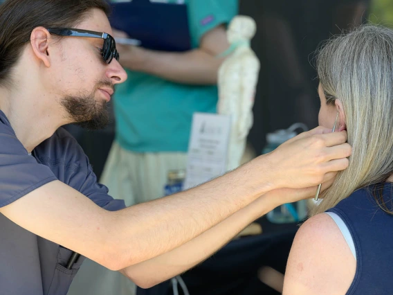 A man attaches a small taped bead to the ear of a woman with long gray hair. 