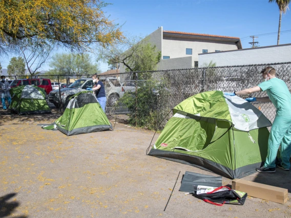 Medical students Christian Bergman (left), Erika Krall, Chris Vance help set up tents at the Z Mansion in downtown Tucson. Homeless individuals with potential or suspected coronavirus infection are isolated outdoors in tents on the property. These makeshift “wards” are staffed by UArizona medical students, who distribute food three times a day and monitor patients for worsening conditions.  