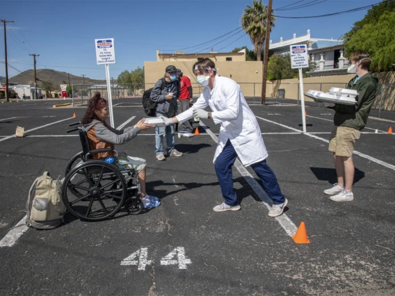 A student in the College of Medicine – Tucson offers food and drink to a woman at Z Mansion, a soup kitchen for homeless people several times a week. They try to keep a safe distance to prevent potential spread of COVID-19 virus.