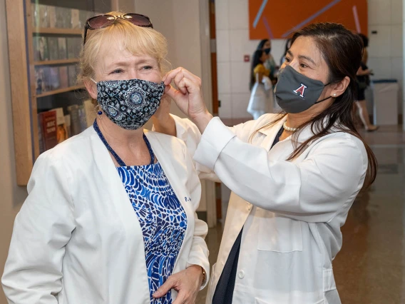 Shu Fen Wung, PhD, MS, RN, ACNP-BC, FAAN, helps Patti Daly, PhD, NP, with a mask adjustment before the white coat ceremony. 