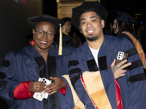 Two smiling nursing students in caps and gowns stand together. 