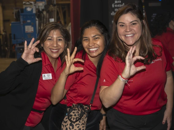 Three smiling women in red polo shirts all make the Arizona Wildcat sign with their fingers. 