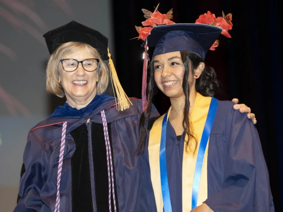 A smiling professor and student stand together in their graduation regalia. 