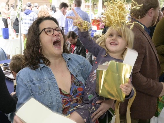 A child tosses crinkle paper into the air from a box while being held by her mom, a fourth-year medical student at the University of Arizona College of Medicine – Tucson, during the Match Day ceremony. 