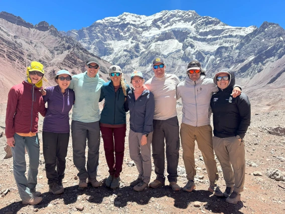 A line of eight men and women stand smiling in front of Aconccagua.