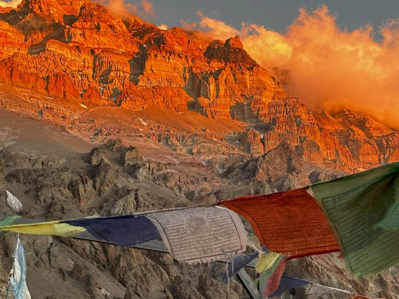 Prayer flags flutter in the wind with mountains and clouds looming in the background.