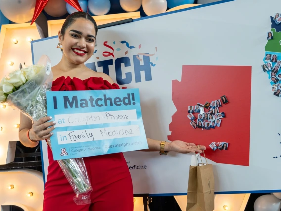 medical student holds a sign indicating her residency match and points to the location on a map