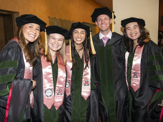 Five University of Arizona College of Medicine – Phoenix students dressed in graduation regalia stand together smiling before their commencement ceremony.