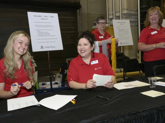 Four University of Arizona College of Nursing staff members work at a check-in table backstage during the convocation ceremony. 