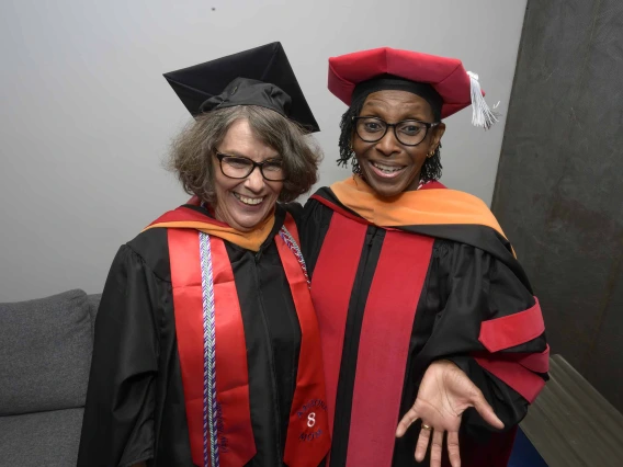 Two University of Arizona College of Nursing faculty members in graduation caps and gowns stand together smiling. 