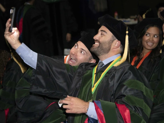 Two University of Arizona College of Medicine – Tucson students in graduation regalia take a selfie before their graduation ceremony. 