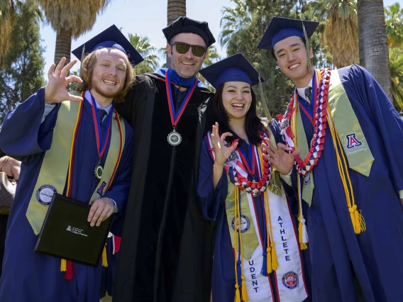 Three University of Arizona R. Ken Coit College of Pharmacy students and one faculty member, all dressed in graduation caps and gowns, stand side by side, smiling. 