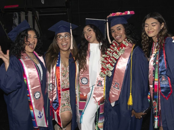 Five University of Arizona Mel and Enid Zuckerman College of Public Health students, all wearing graduation caps and gowns, smile and wave. 