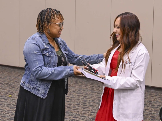 A University of Arizona College of Medicine – Phoenix staff member hands a book to a new medical student. Both are smiling. 