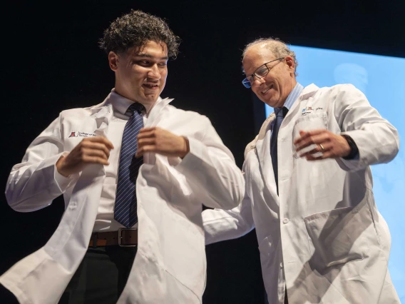 A University of Arizona College of Medicine – Tucson student adjusts a medical white coat that was just put on him by a professor.