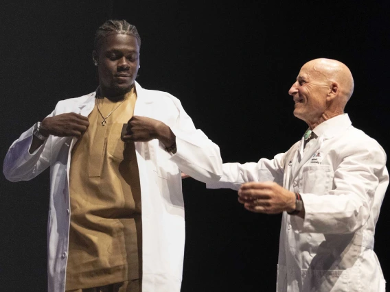 A University of Arizona College of Medicine – Tucson student adjusts a medical white coat that was just put on him by a professor.