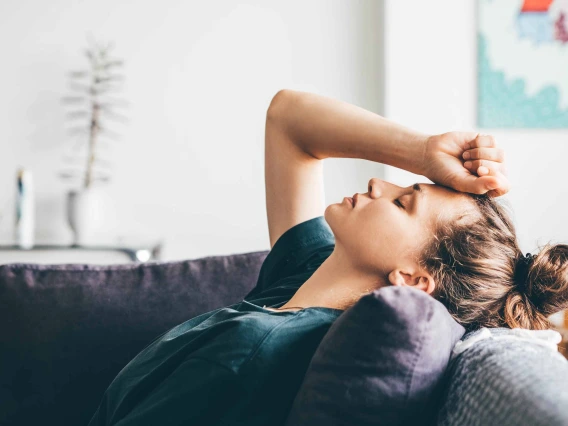 Person laying on a couch with arm raised and hand on forehead 