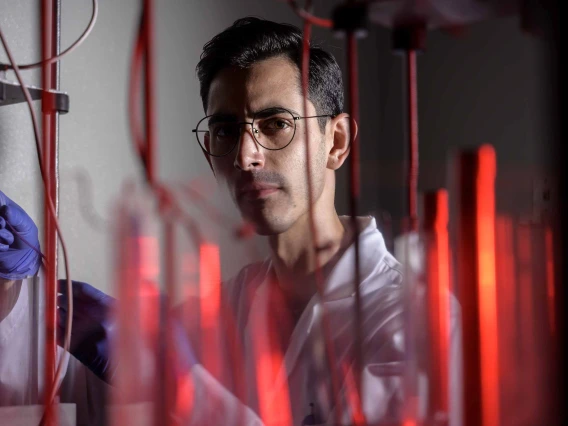 Portrait of research scientist Robson Vizin looking through red lab tubes. 