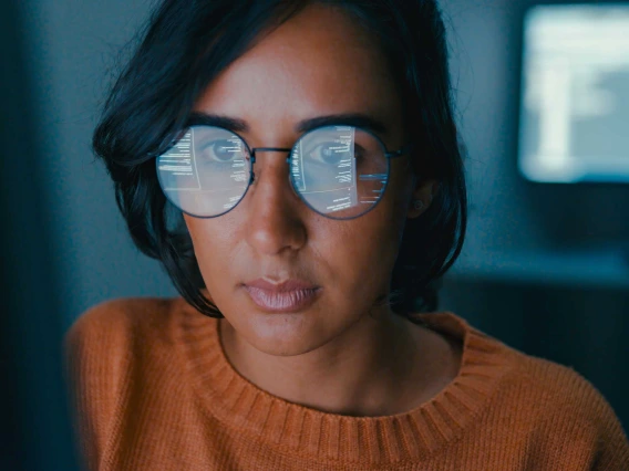 A photo illustration of a woman looking at a computer screen with words and numbers reflected in her glasses. 