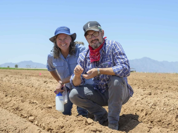 Two researchers crouching near a row of freshly tilled dirt in an agricultural field