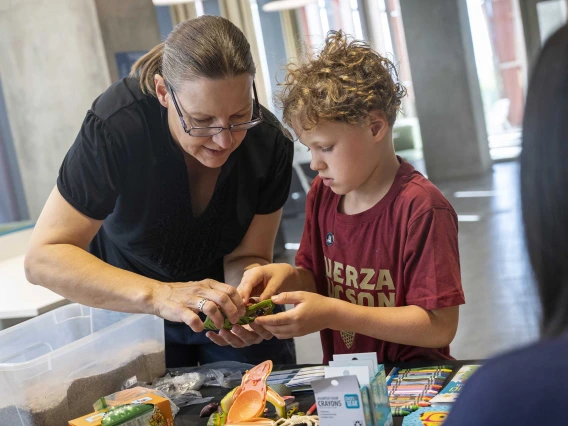 A mother and son stand at a table working on a plastic, 3D puzzle of a frog. 