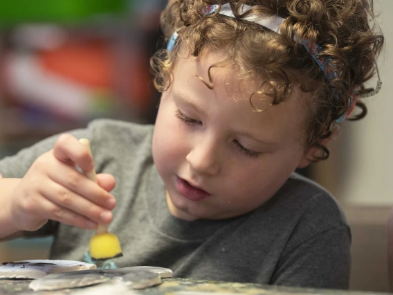 A young girl focuses intently as she paints an art project. 