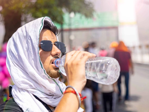 A photo illustration of a man drinking water and covering his head while exposed to extreme heat