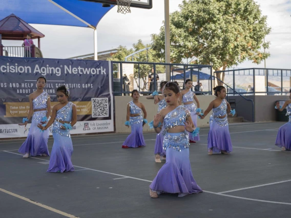 Several young dancers in dresses perform in an outdoor setting. 