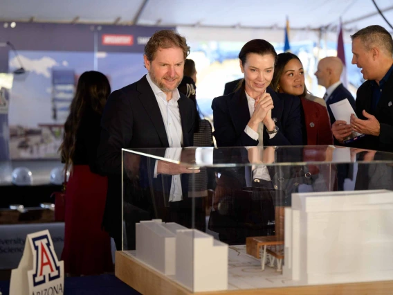 A man and woman smile as they look at a 3-D building model in a glass case. 