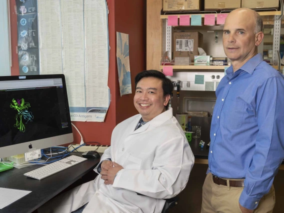 Two immunologists, one seated and one standing, pose in a University of Arizona Health Sciences research laboratory