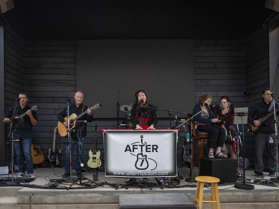 Photo of a line of musicians outside on a stage with a logo reading the band’s name, After 7.