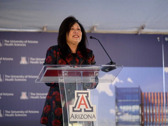 Cecilia Mata, chair of the Arizona Board of Regents, dressed in a dark blazer, stands at a lectern with the University of Arizona logo on it. 