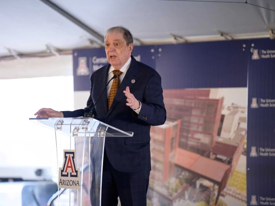 Michael D. Dake, MD, senior vice president for the University of Arizona Health Sciences, wearing a dark suit, stands on a stage at a clear lectern with the U of A logo on it.  