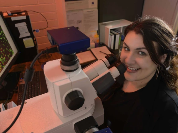 Portrait of a woman looking up from a microscope and smiling.