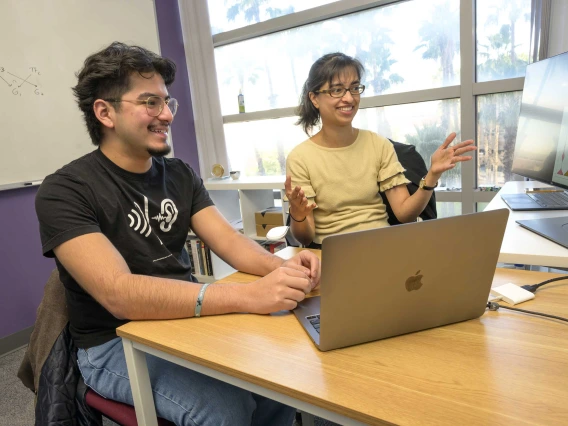 A student and faculty mentor sit at a desk looking at a computer monitor