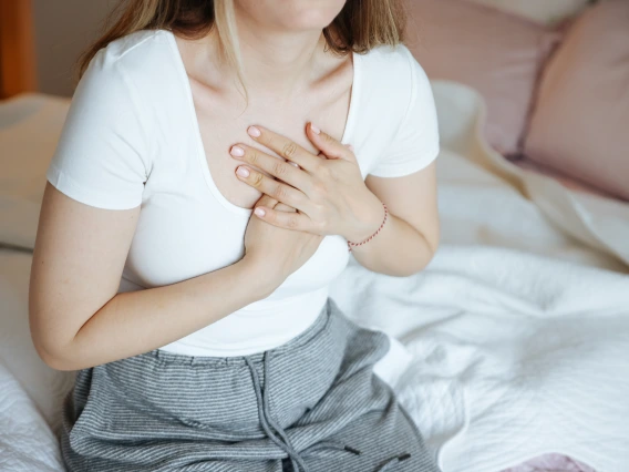 A young woman clutches at her chest while sitting in bed.