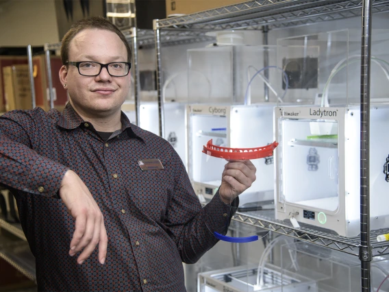 Tory Middlebrooks, of University Libraries, holds a face shield, which is designed to be worn in conjunction with addition PPE such as a mask. Middlebrooks runs the 3D printers that produced the headbands for the face shields created by University of Arizona employees and students inside makerspaces across campus. The effort was well underway in early April.