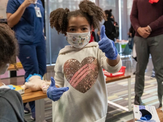 Little girl tries on gown and gloves at the Wildcat Play Hospital sponsored by the University of Arizona College of Nursing.