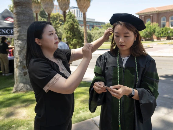 Lydia Lee (left) helps her sister, Eun Hye Lee, MD, with her cap before the start of the College of Medicine – Tucson class of 2022 convocation at Centennial Hall. 