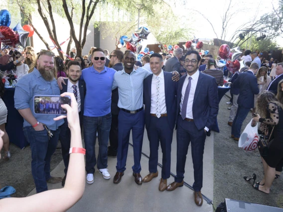 Six young adult men stand side by side with arms around each others shoulders. 