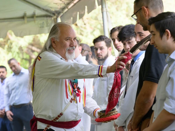 An older man in a traditional Native American designed shirt touches the forehead of a young man with an eagle feather. 